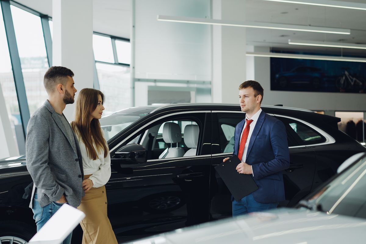 Salesperson helping a couple beside a new SUV in a bright car dealership showroom