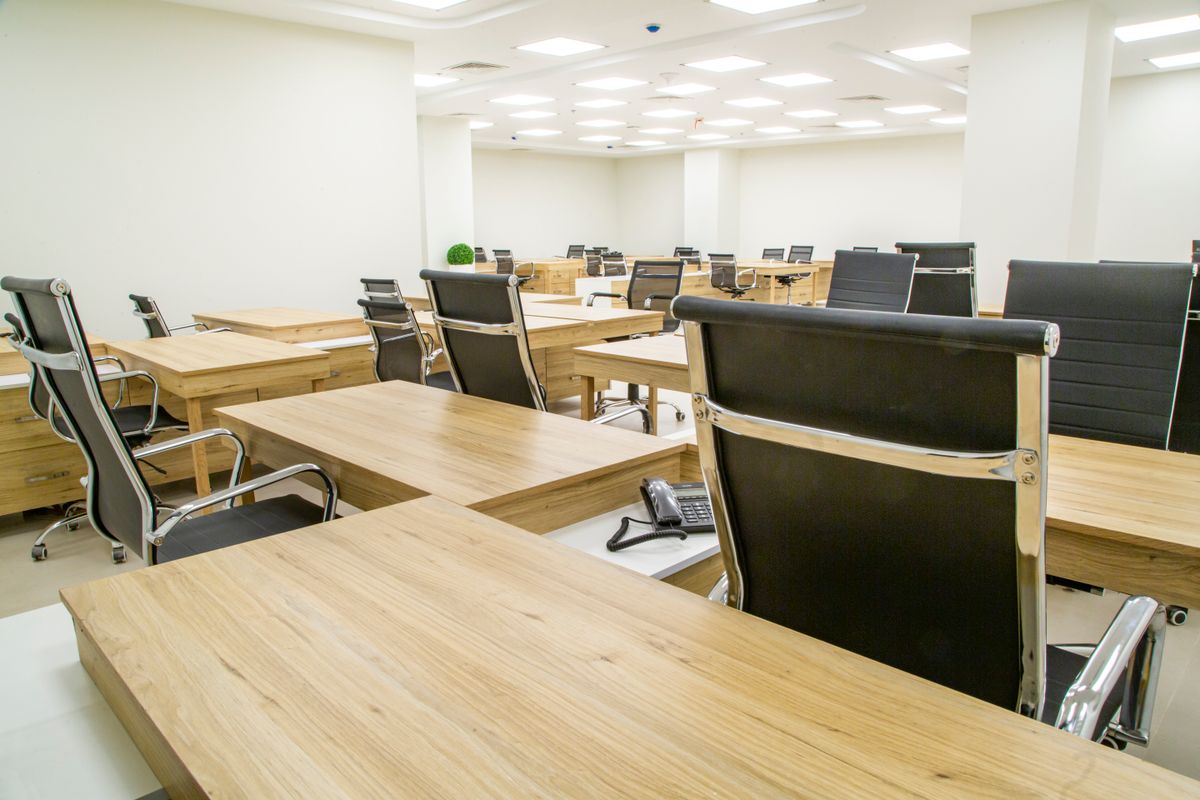 Bright, clean open office with wooden desks and black chairs, ready for the next workday