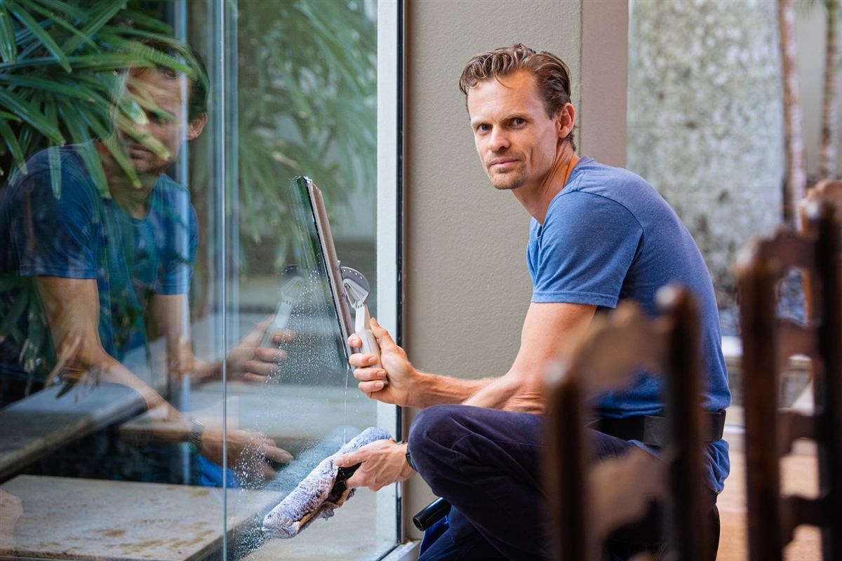 Professional cleaner holding a squeegee beside a glass wall
