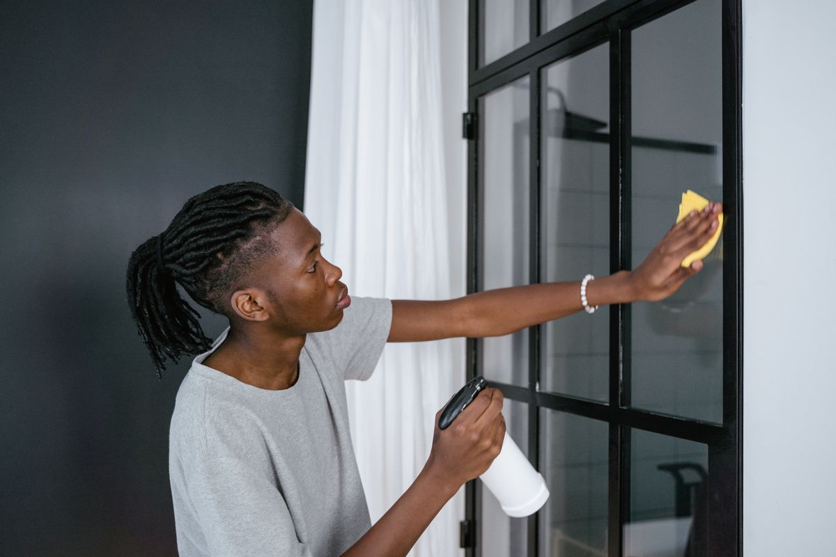 Person cleaning an interior glass partition with a spray bottle and a cloth