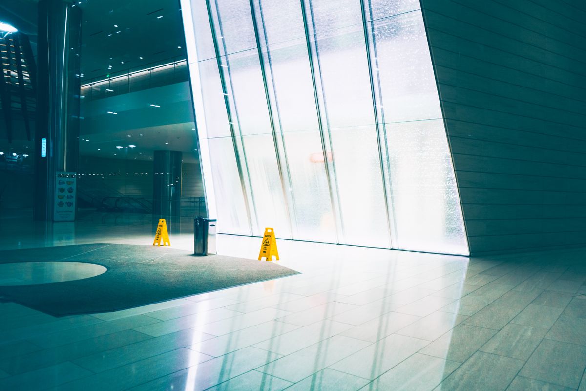 Bright office building lobby with yellow wet floor signs beside a glass wall, the kind of entrance a day porter keeps safe and presentable