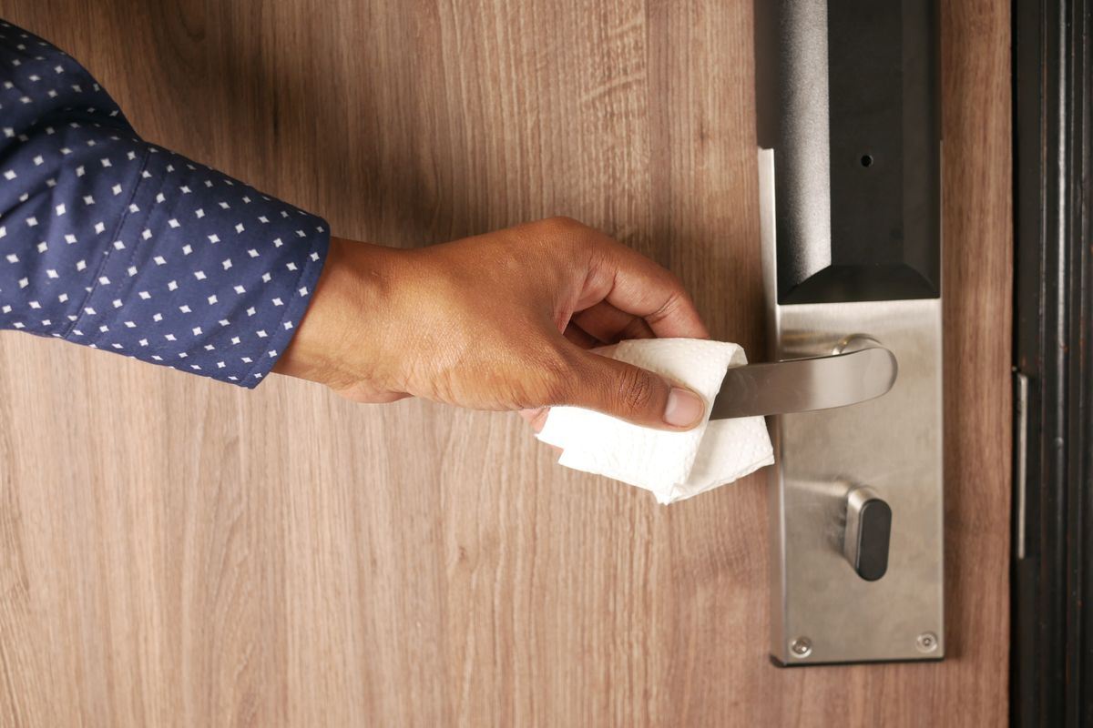 Hand wiping a metal door handle to disinfect a high-touch surface