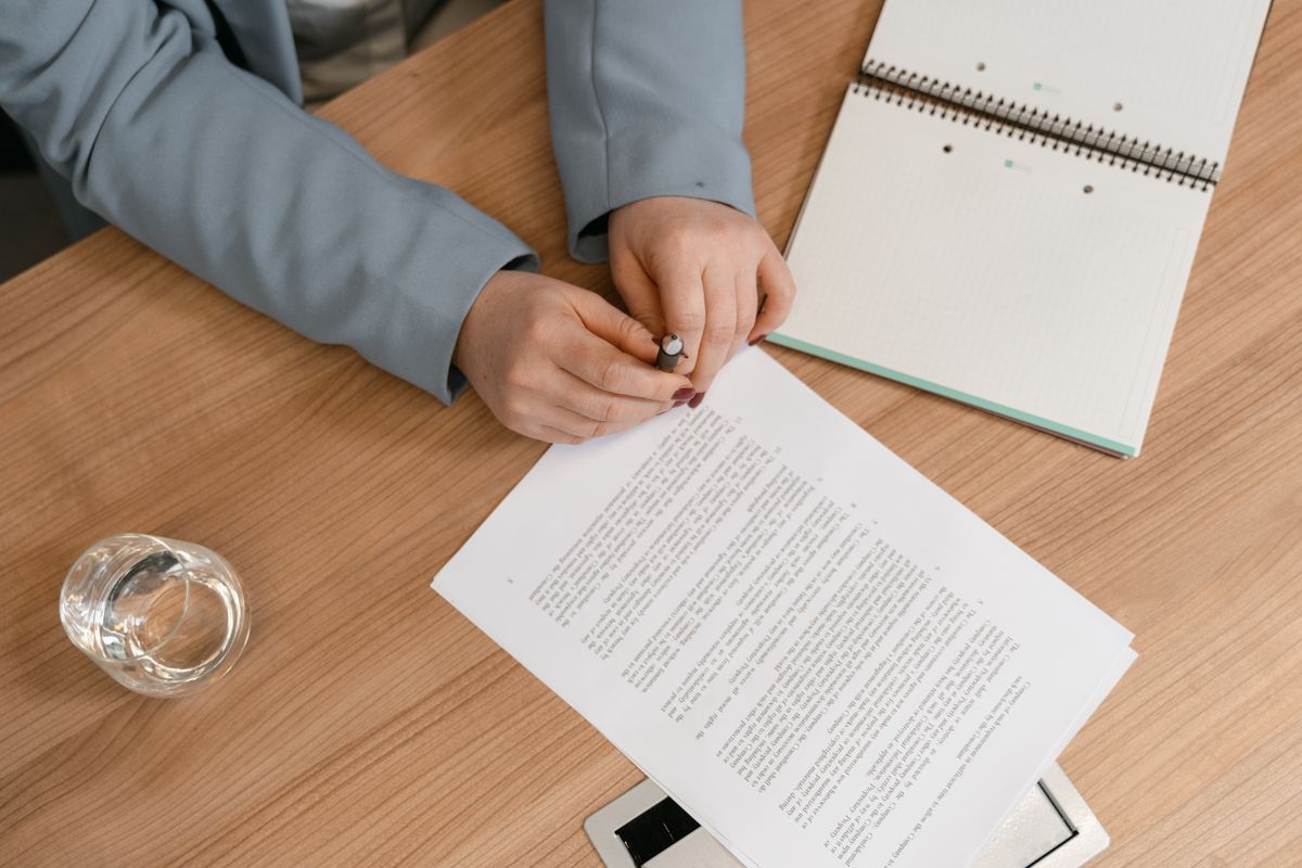 Office manager at a wooden desk reviewing a printed service proposal with a pen and notebook