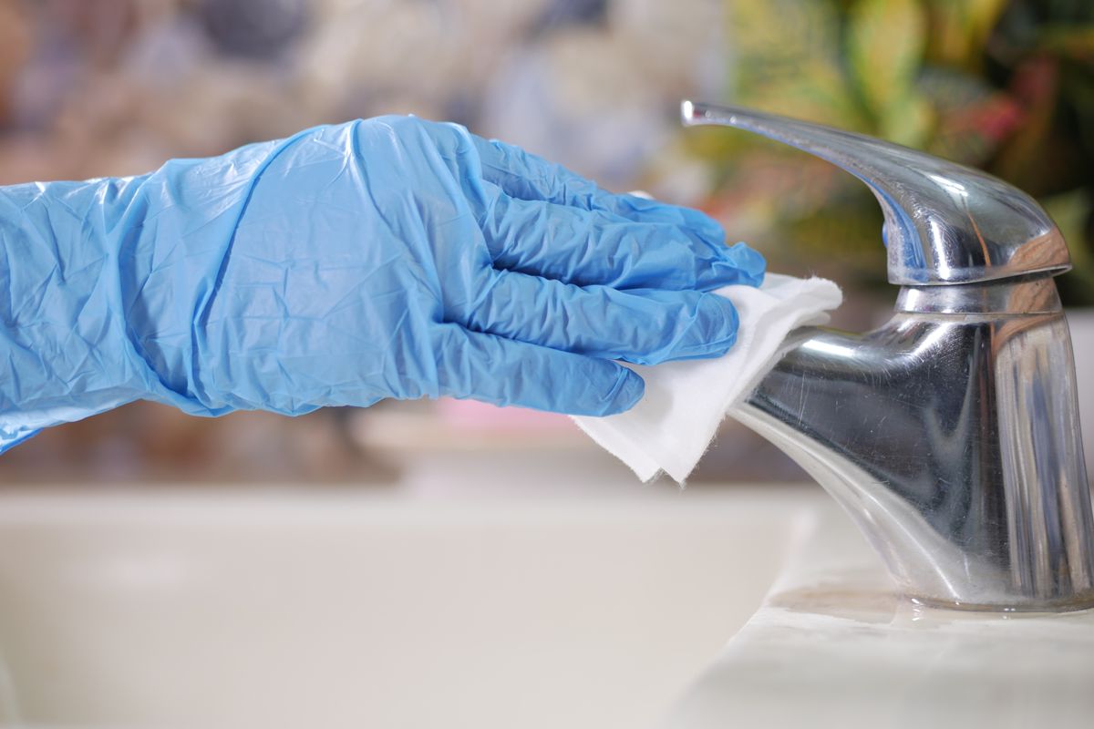 Gloved hand wiping a restroom faucet with a cloth